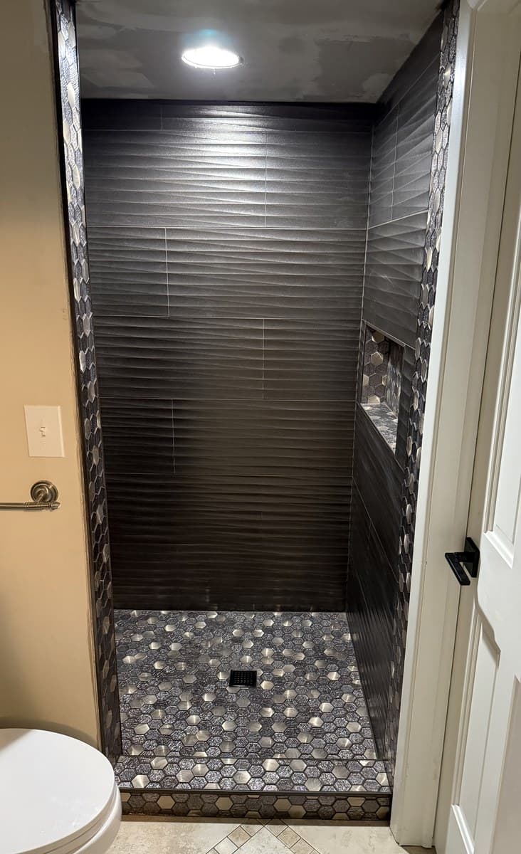 Bold dark walk-in shower with charcoal ribbed horizontal tile walls, hexagon pebble mosaic floor, and recessed lighting in Lake County Ohio
