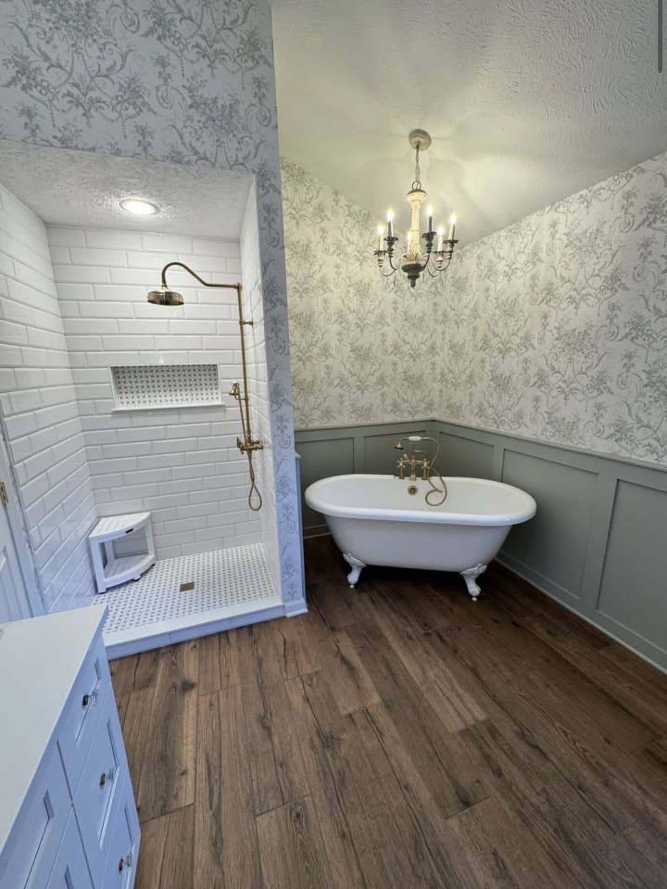 Complete master bathroom renovation with white subway tile shower, brass gold fixtures, clawfoot soaking tub, chandelier, and botanical wallpaper in Lake County Ohio