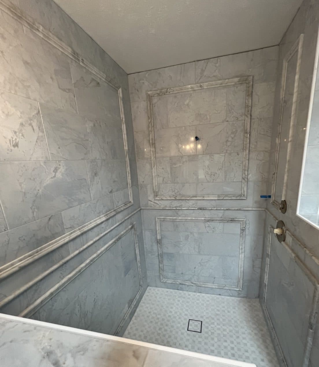 Walk-in shower remodel with full marble tile surround, two framed niches, and hexagon mosaic floor in Cuyahoga County