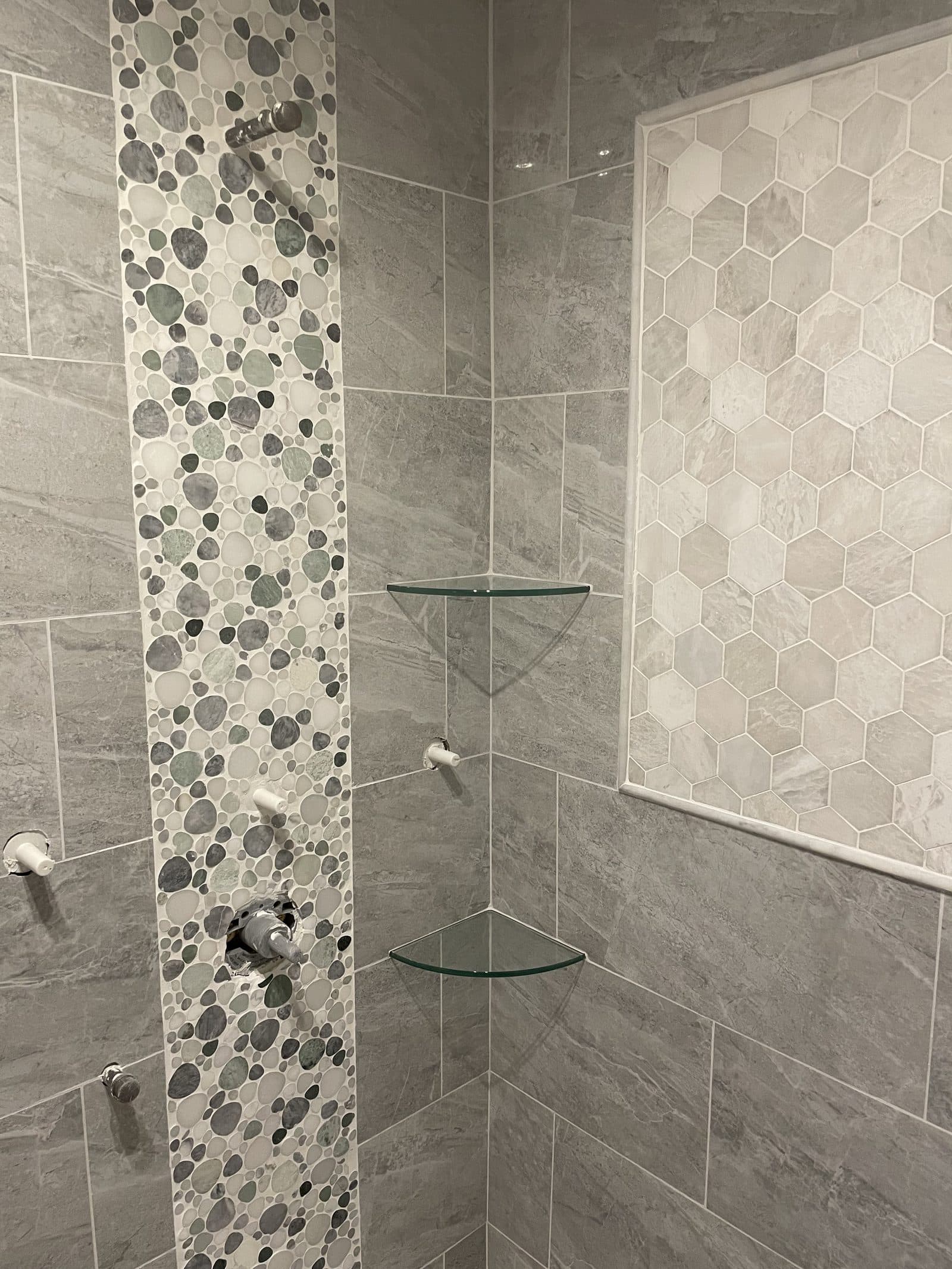 Shower remodel with gray stone large-format tile walls, pebble mosaic accent strip, hexagon mosaic niche, and glass corner shelves in Northeast Ohio