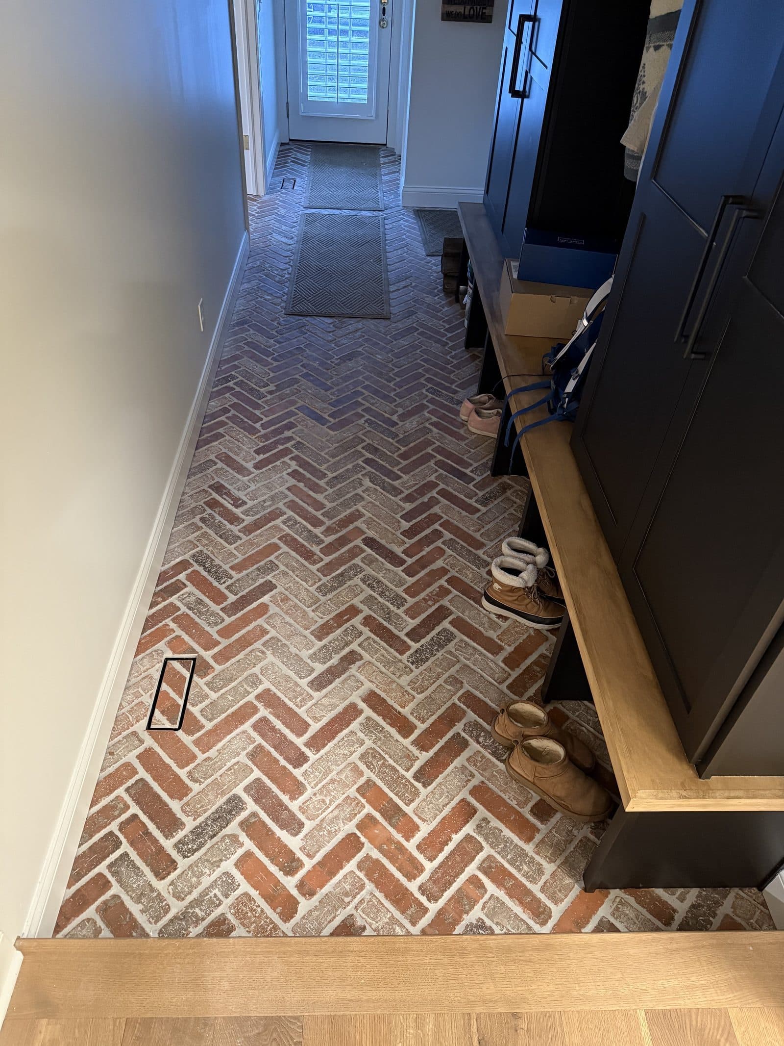 Red brick herringbone mudroom and entryway floor tile installation with dark built-in cabinetry in Lake County Ohio