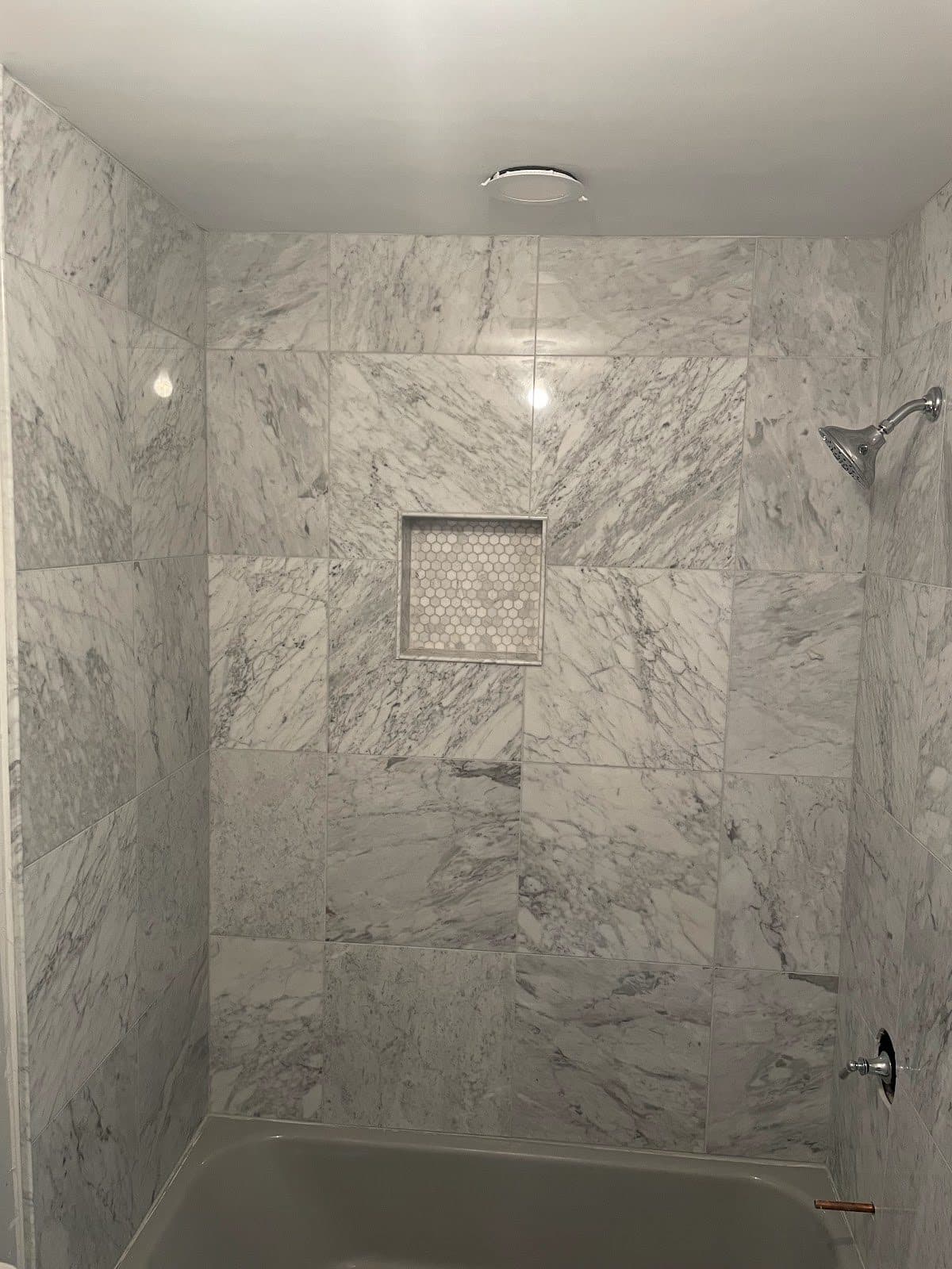 Full Carrara marble shower and tub surround with large-format marble tiles and hexagon penny mosaic niche in Lake County Ohio