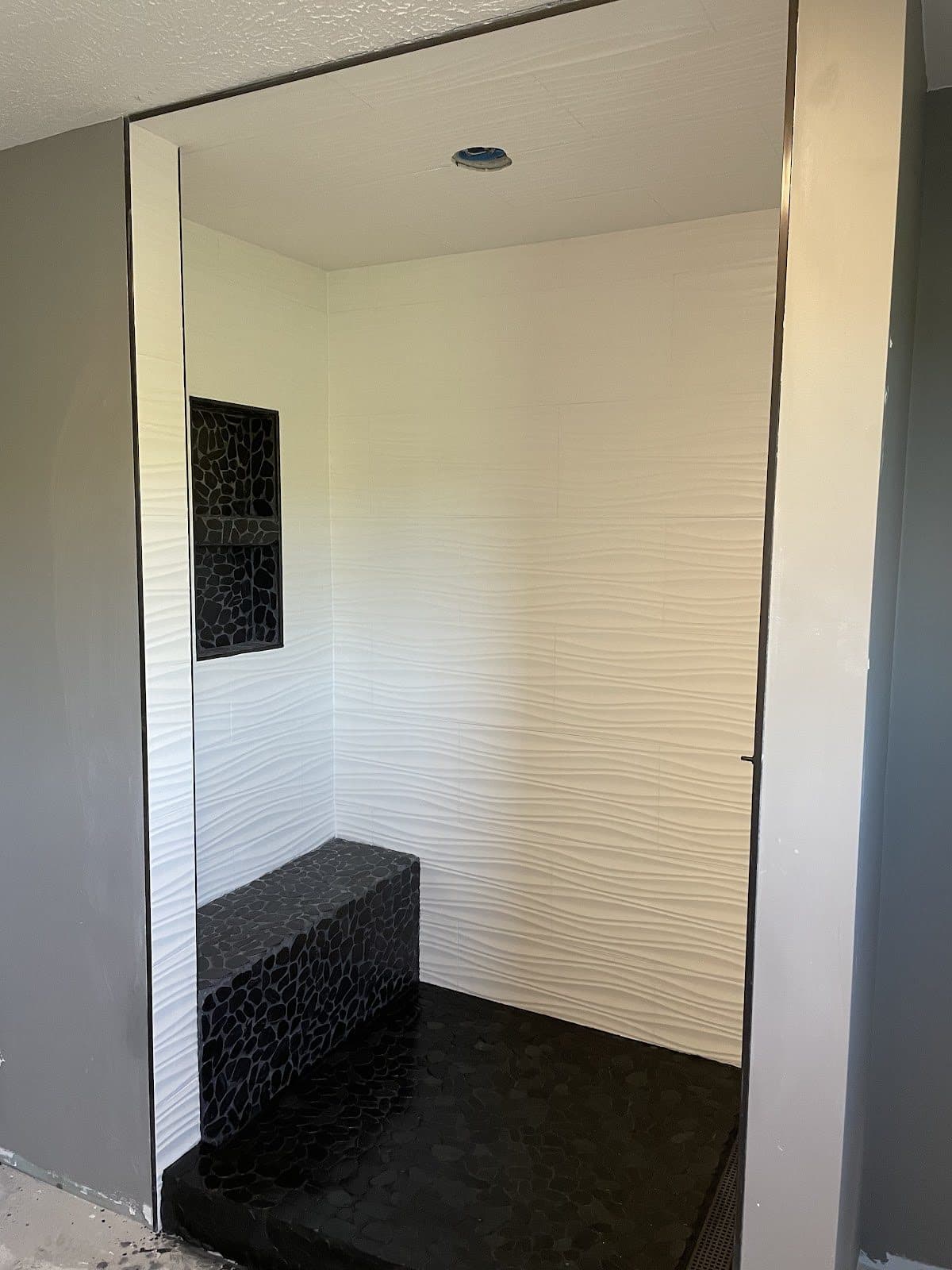 Walk-in shower with white wavy 3D tile walls, black pebble mosaic bench, and custom built-in niche in Northeast Ohio